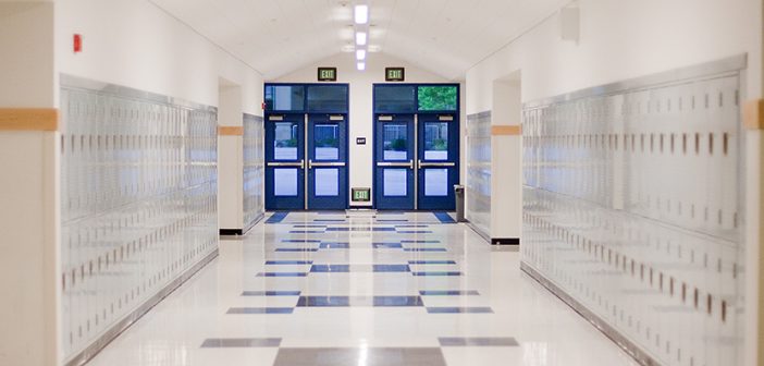 brightly lit school hallway with light gray lockers and blue doors with window leading outside